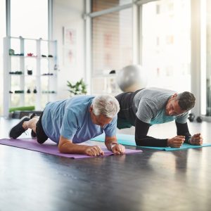 personal trainer exercise elderly man with plank mobility support training retirement lesson instruction physio with help floor recovery rehabilitation joint strength