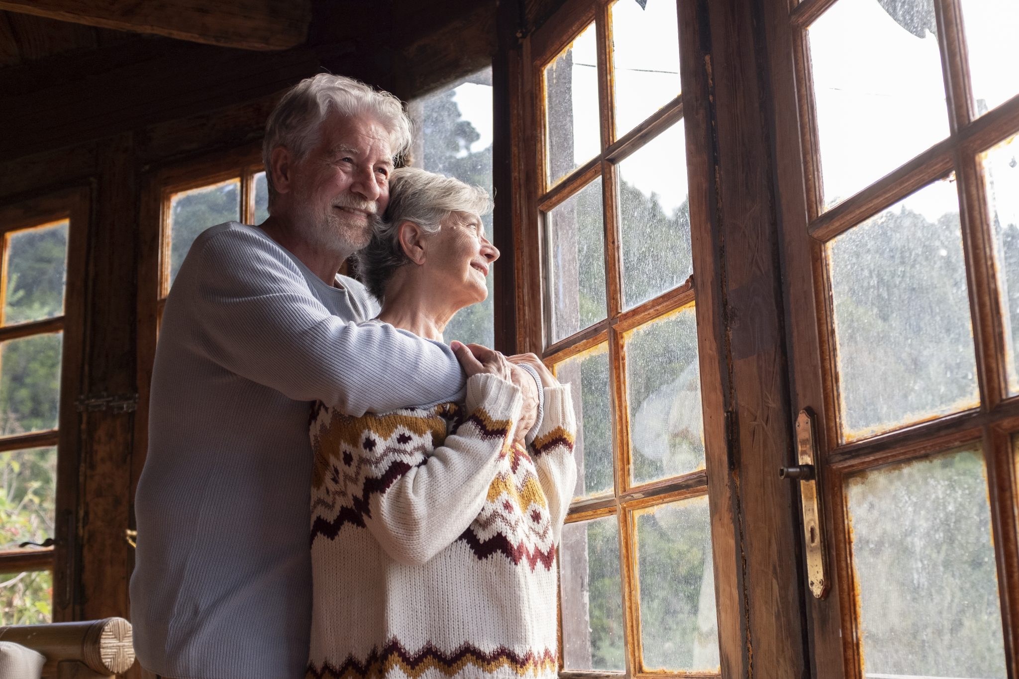 senior couple embracing standing by window scaled